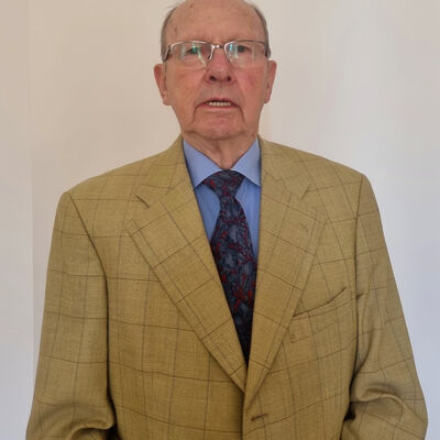 Ein älterer Herr mit Brille in einem ockerfarbenen Anzug.
