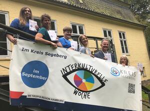 Fünf Frauen und Landrat Schröder halten ein weißes Plakat hoch. Sie stehen auf einer Treppe - direkt vor einem Geländer.