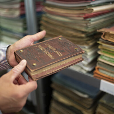 Ein Mitarbeiter hält ein historisches Buch aus dem Kreisarchiv in den Händen. Im Hintergrund sieht man ein Regal mit älteren Akten.